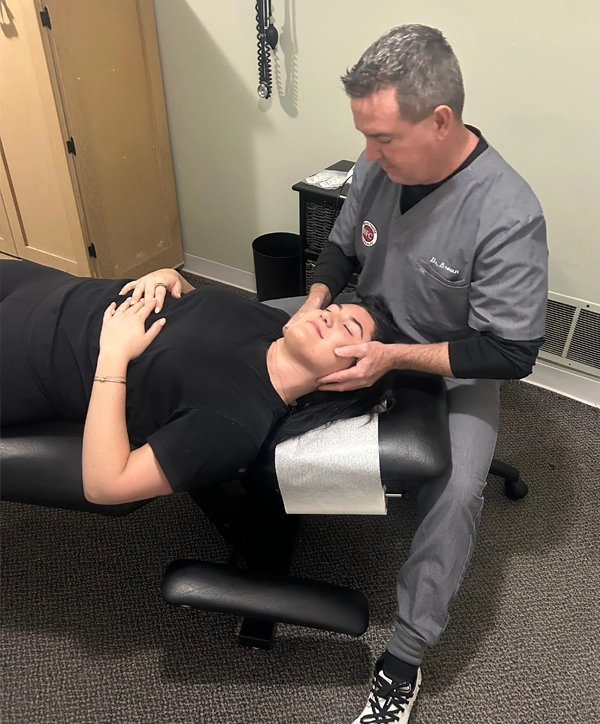 Chiropractor Christopher Brown performing a neck adjustment on a smiling patient.