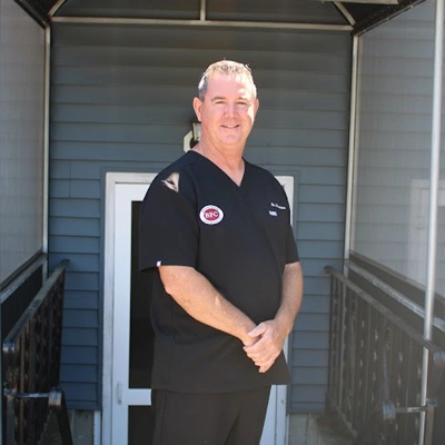Chiropractor Christopher Brown smiling out side of clinic in black scrubs.